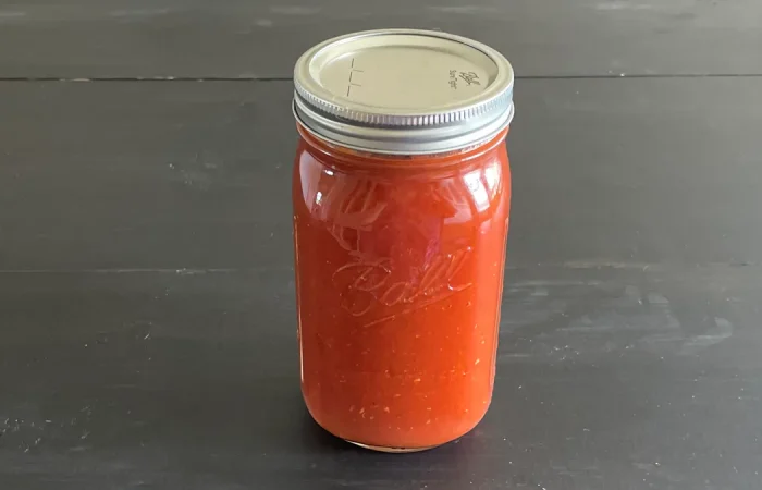 Mason jar of vodka sauce that has been canned sitting on a dark surface.