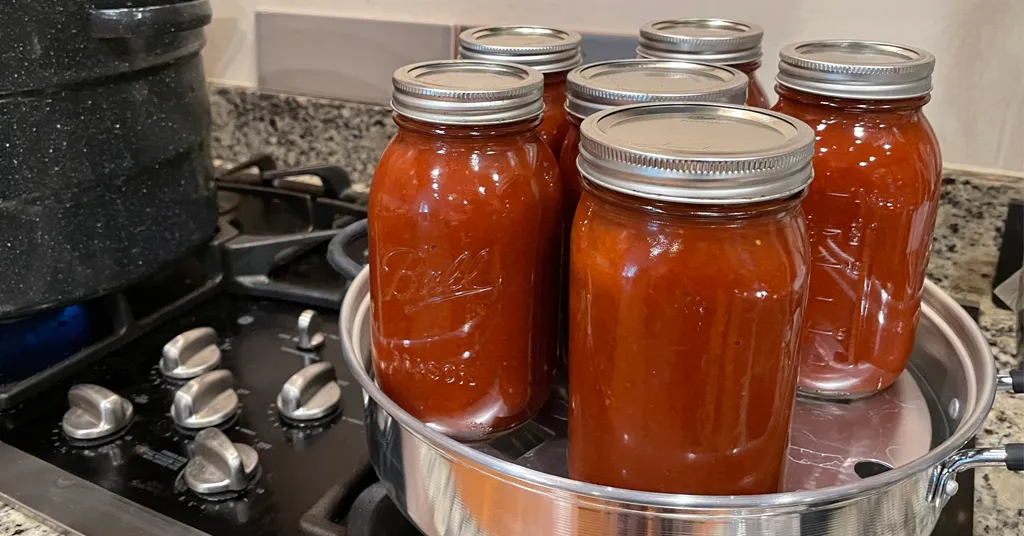 Six mason jars of Vodka Sauce being canned in a steam canner with a water bath canner near by.