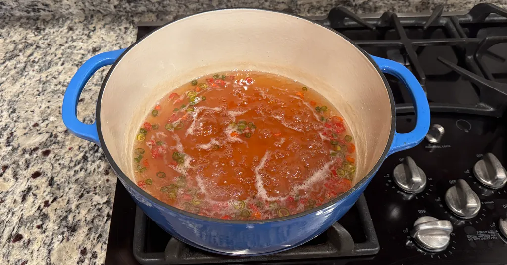 Large enameled Dutch oven full of apple jalapeno jelly cooking on a stove.