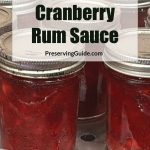 This image shows glass jars filled with homemade cranberry rum sauce, neatly sealed and arranged on a canning rack. The overlay text reads, "How To Can Cranberry Rum Sauce" with a website link, PreservingGuide.com, showcasing the process and recipe for preserving this spiced, fruity condiment.