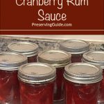 This image shows multiple jars of homemade cranberry rum sauce placed on a steam canning rack. The background text reads, "How To Steam Can Cranberry Rum Sauce" from PreservingGuide.com, emphasizing the method and guide for preserving this sweet and tangy sauce.