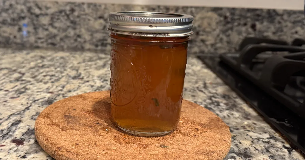 Mason jar of Apple Jalapeno Jelly sitting on a cork coaster on a kitchen counter.