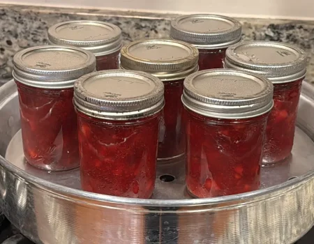 Seven mason jars of strawberry jam sitting in a steam canner.