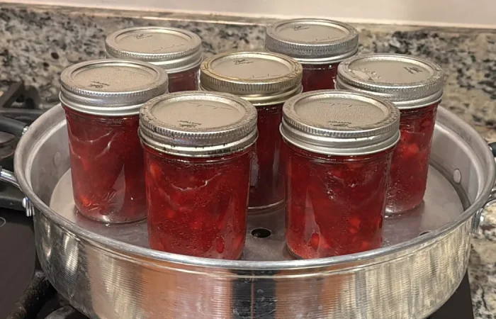 Seven mason jars of strawberry jam sitting in a steam canner.