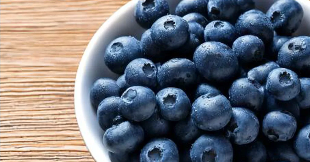 Blueberries in a white bowl sitting on a wooden counter.