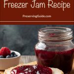 Image of a jar of blueberry raspberry freezer jam next to a slice of bread topped with glistening red jam, placed on a wooden surface. A small bowl of fresh blueberries and raspberries is visible in the background. The text overlay at the top reads: 'Blueberry Raspberry Freezer Jam Recipe - PreservingGuide.com.'