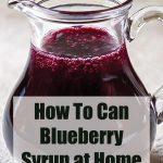 A clear glass pitcher filled with dark, rich blueberry syrup, with a text overlay reading 'How To Can Blueberry Syrup at Home' and the website name 'PreservingGuide.com' at the bottom. The syrup has a glossy finish, reflecting light, and the background is softly blurred for emphasis.