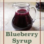 A glass pitcher filled with homemade blueberry syrup, sitting on a textured surface, with a blurred jar of blueberries in the background. The text overlay reads 'Steam Canning Blueberry Syrup' in bold, classic fonts, framed by a burgundy border, and a decorative jar icon is featured at the bottom. The design has a clean, rustic aesthetic with a beige backdrop.