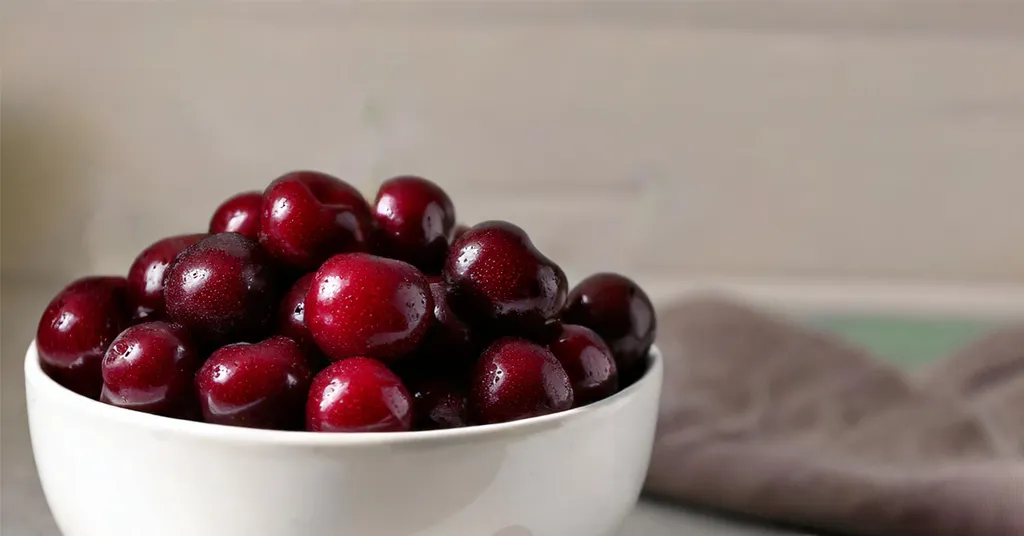 Dark red cherries in a white bowl sitting on a counter.