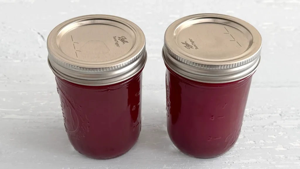 Two mason jars full of cranberry juice sitting on a light blue wooden surface.