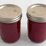 Two mason jars full of cranberry juice sitting on a light blue wooden surface.