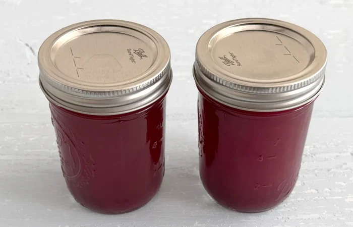 Two mason jars full of cranberry juice sitting on a light blue wooden surface.