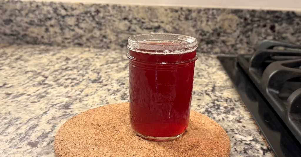 Mason jar sitting on a cork trivet filled with cranberry juice.