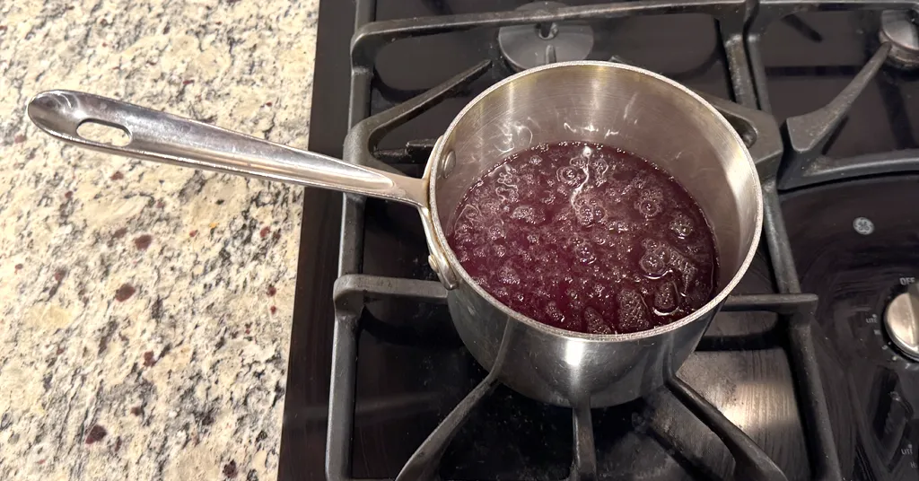 Pot sitting on a stove with boiling cranberry juice.