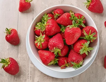 Ripe red strawberries in a white bowl with strawberries spread out on the counter around the bowl.