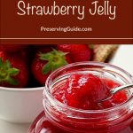 An open glass jar filled with thick, glossy strawberry jelly, with a spoon scooping out a portion. Fresh strawberries in a white bowl and a woven basket are visible in the background. The top of the image features a brown banner with white text reading, 'How To Can Strawberry Jelly,' along with the website 'PreservingGuide.com' below.