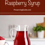 A glass pitcher filled with deep red raspberry syrup sits on a kitchen counter, surrounded by fresh raspberries and a white bowl in the background. The top of the image features a dark red banner with the text “How To Can Raspberry Syrup – PreservingGuide.com.”